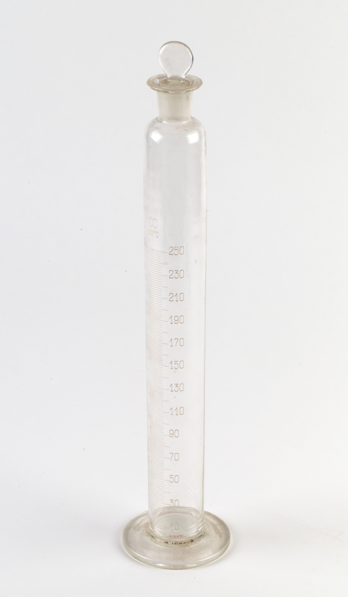 Målesylinder med glasspropp fastbundet med hyssing rundt sylinderens hals.
Inngravert gradering med tall fra 10 til 250.