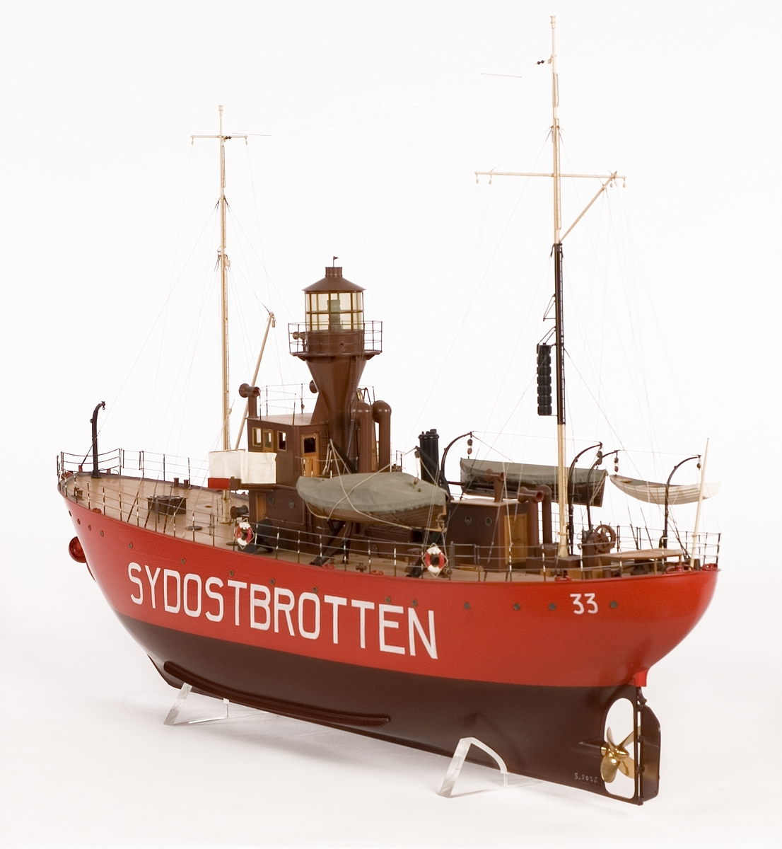 Fartygsmodell av fyrskeppet SYDOSTBROTTEN styrbords sida öppen, visande inredning. Fyrtorn med plattform runt lanterninen. Två master, tre båtar och ett skålankare i centralt stävklys.