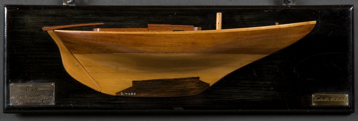 Halvmodell av kuttern BRIS. Styrbords sida, en mast, ruff, sittbrunn. Monterad på svart träplatta.