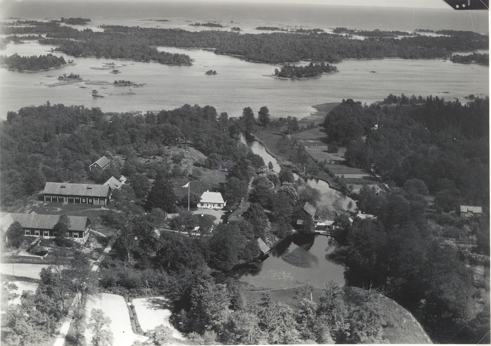Flygfoto över Virbo med hus och ekonomibyggnader samt grusvägen och sjön i bakgrunden.