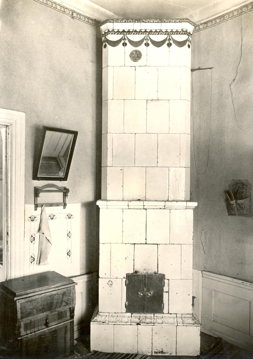 Huvudbyggnaden; kakelugn i kökskammaren, sannolikt Mönsteråsfabrikation från 1800-talets förra hälft. Sockellist med reliefdekor. Krönet med målad dekor.