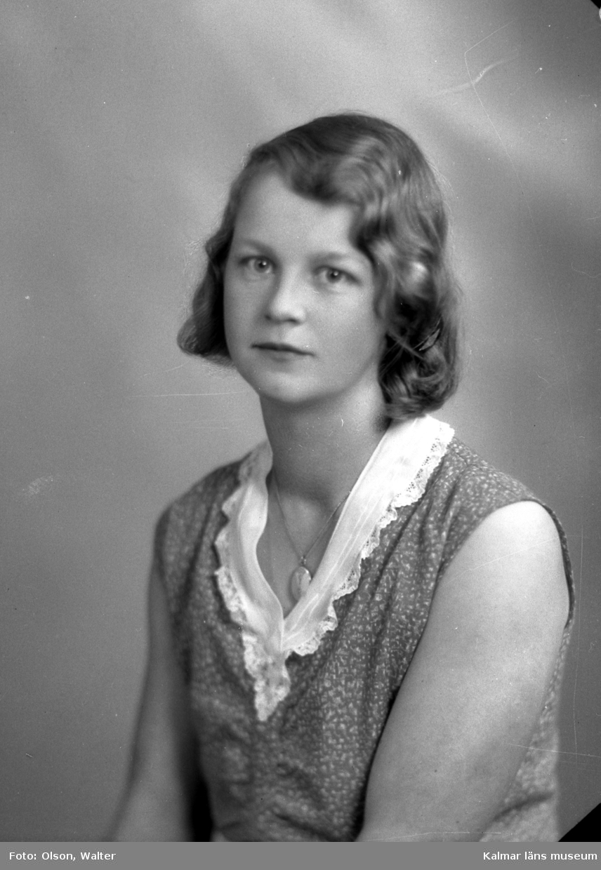 Ateljébild på en kvinna i klänning och medaljong. Enligt Walter Olsons journal är bilden beställd av Ragnhild Jakobsson.
