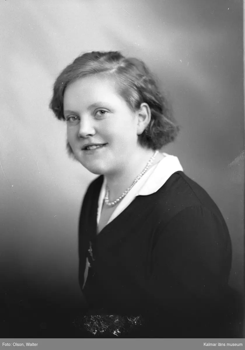 Ateljébild på en kvinna i pärlhalsband. Enligt Walter Olsons journal är bilden beställd av Frida Johansson.