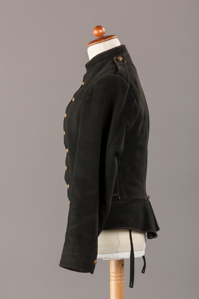 Form: Enkeltspent.

Foret med lin. Forsterket med silke på et lite stykke på ryggen. 12 messingknapper med mønster og tallet 1. Hempe i lin. Bendelbånd med knappehull.