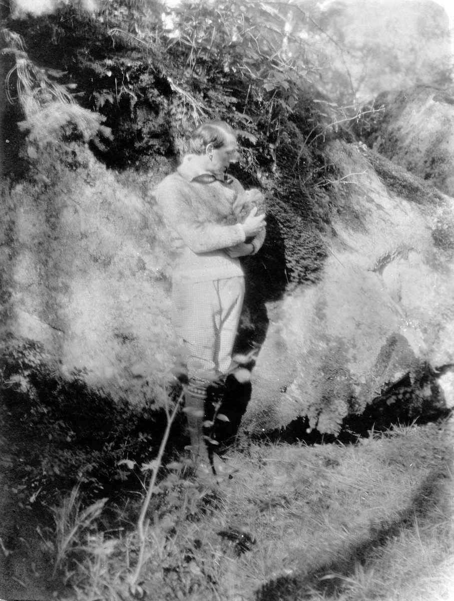 John Bauer i skogen framför en grotta med en trolldocka i famnen vid Björkudden utanför Gränna.