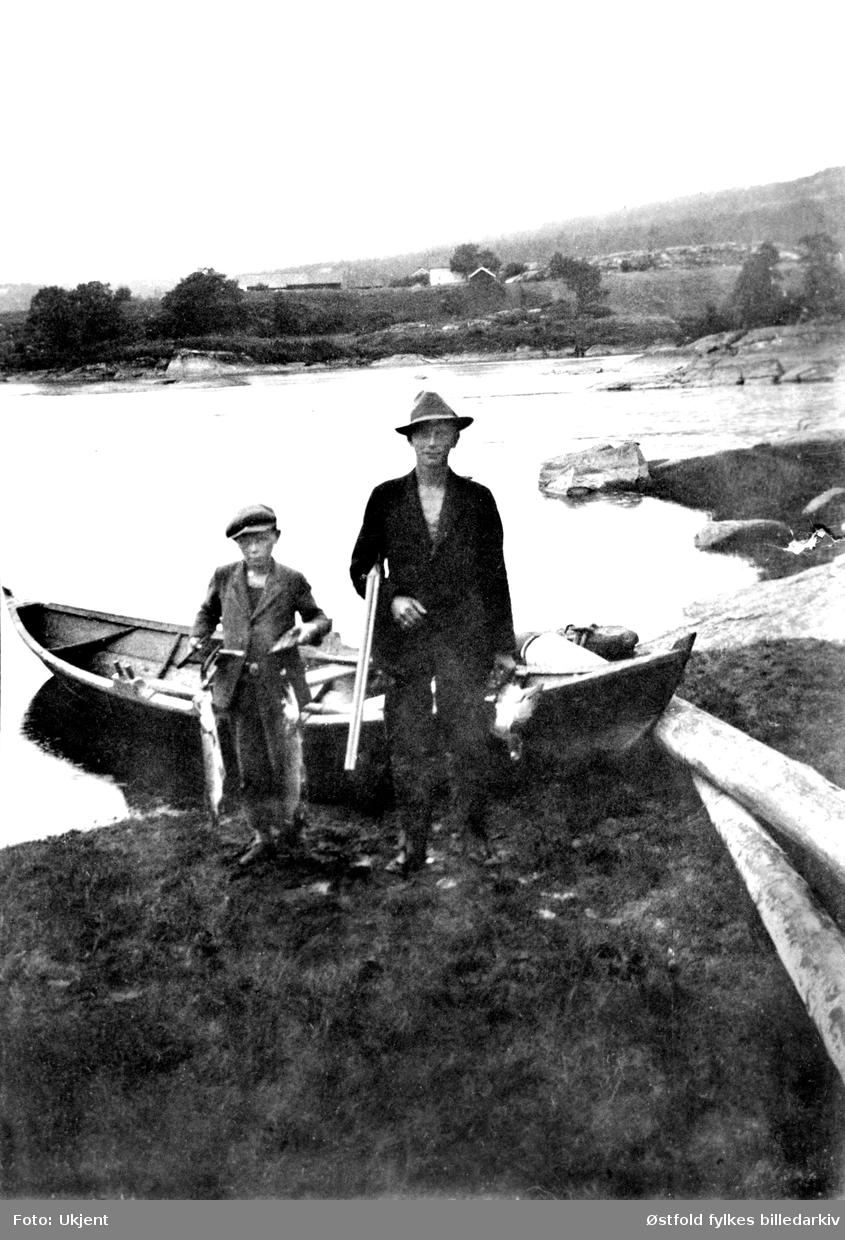 På fisketur i Glomma ved gården Lunde i Varteig ca. 1932.  Fra venstre: brødrene Johan og Arthur Lunde. Man brukte geværet til å skyte gjedde.
