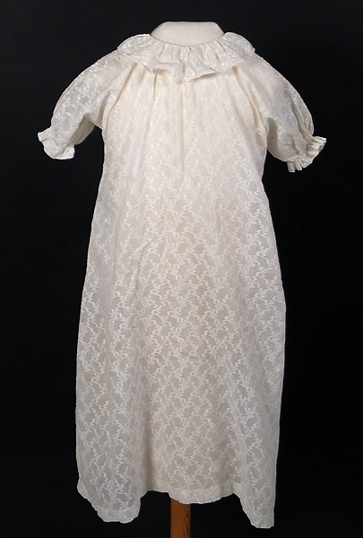 Vit dopklänning sydd av ett tunt, mönstervävt bomullstyg. Sprund bak, som knäppts med hake och hyska. Endast de två sydda hyskorna är kvar. Hakarna var sannolikt av metall, rostfläckar finns.

Dopklänningen har använts av ägarnas 6 barn, födda mellan 1905-1922