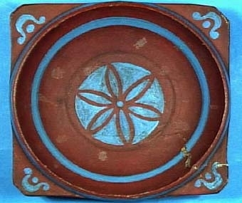 Snibbskål med sentida målning i rödaktigt brunt med blå, geometrisk dekor på utsidan. Under bottnen är utskuret ett "A".