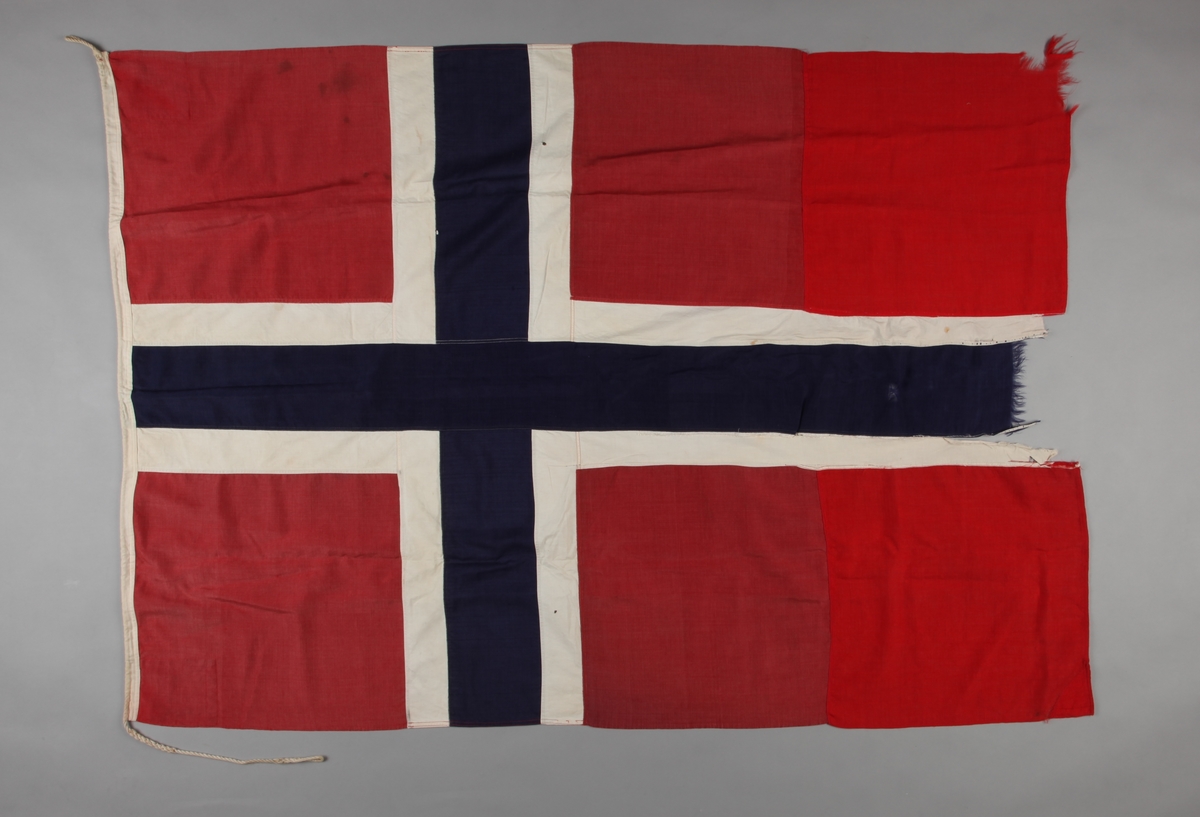Norsk flagg fra DS DRAUGEN. Skader særlig på enden med hvitt og blått felt. Deler av rød tekstil er satt inn senere.