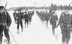 Menn, uniform, geværer, ski og skistaver, naturforhold. 
Fr