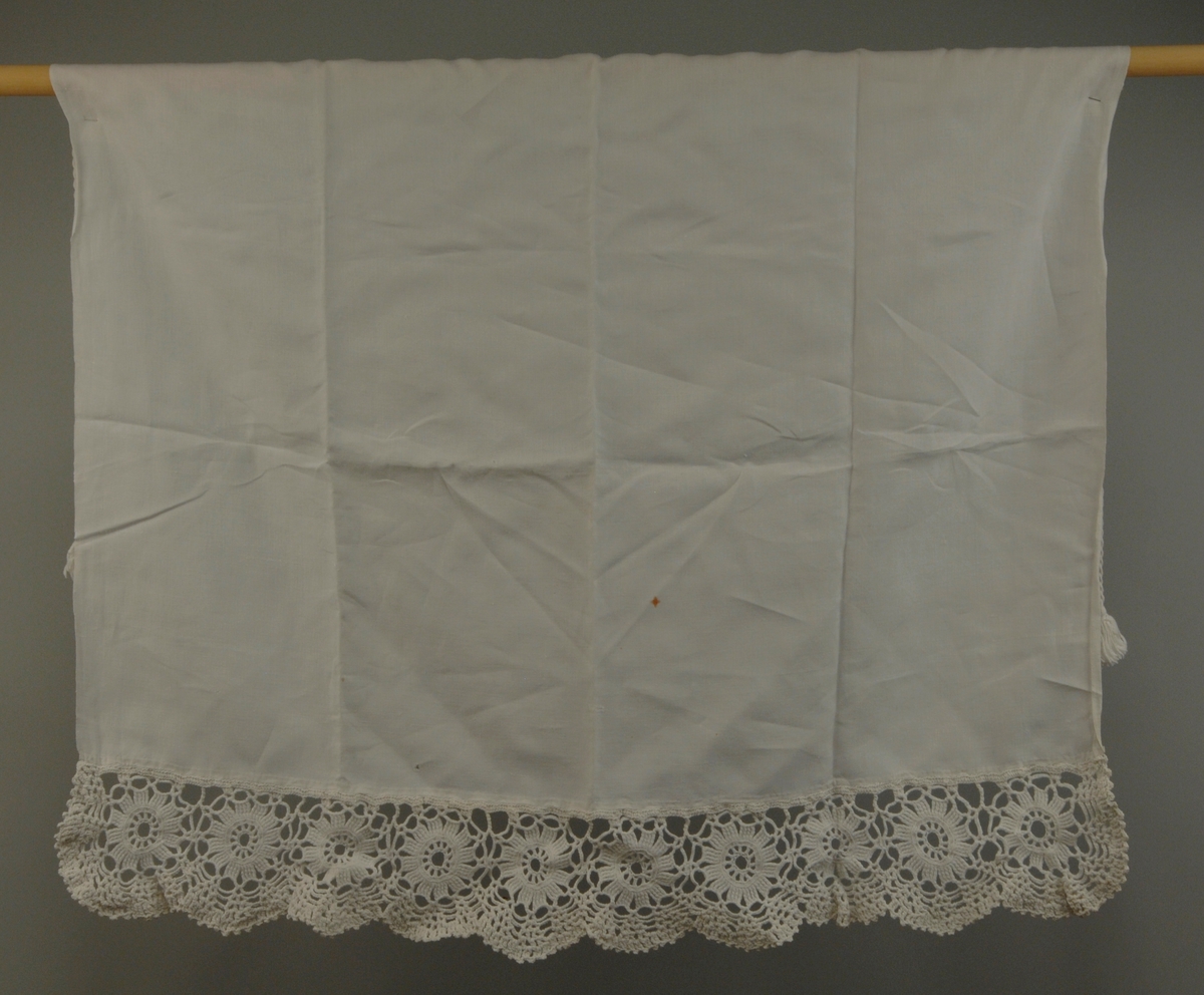 Forkle går fra livet og ned. I øvre kanten er det sydd en løpegang for bånd, ca. 1 cm brei. Ei tvunnet bomullssnor med dusker i endene er tredd inni løpegangen. Nedentil er stoffet faldet for hånd og påsydd ein håndhekla blonde i tykt bomullsgarn, det består av 10 sirkler med blonde rundt. Blonden er tunget nedentil.