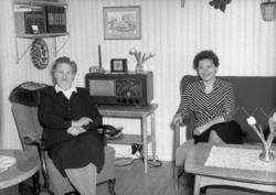 Foto av to kvinner sittende i en dagligstue. Bildet er regis