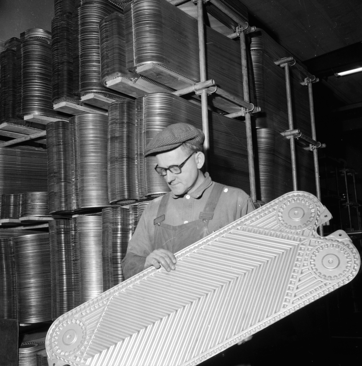 Lingbo verkstäder.
Erland Hansson visar en"trettiotvåans platta" till värmeväxlare. De stansas i Rosenblads verkstad i Ulfsunda i en press, som är Skandinaviens största i sitt slag. Trycket är på 12,000 ton och pressningen sker mot en hårdgummiplatta för att få "mjuka" kurvor i godset.
13/11 1958