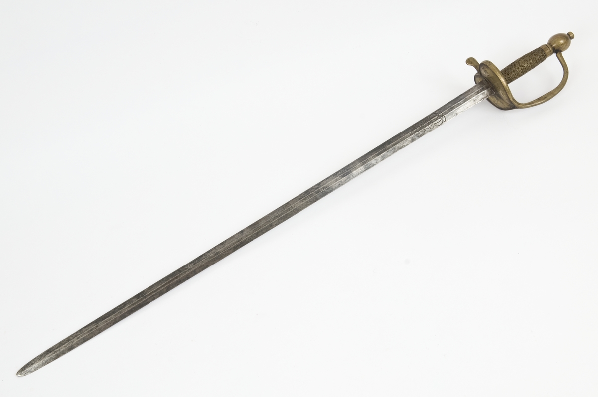 Offiserskorde dansk/norsk modell 1710. Messingfeste. Plommeformet knapp med nitteknapp. Hjerteformede parerplater, Fremre parerstang går over i håndbøylen som er tappet inn i knappen, rett bakre parerstang som ender i en flattrykt dråpe. Tvunnet messingtråd grep med messingbånd avslutning oppe og nede. Tveegget, sekskantet, rett klinge. Christian VI kronede speilmonogram på begeg sider av klingen.