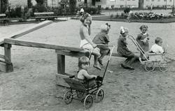 Barn på dumphuske og sittende i barnevogn ved en grusbelagt 