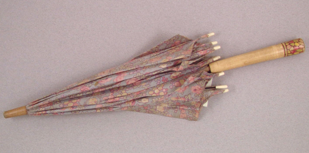 Ett parasoll, leksaks- av blommigt bomullstyg på trästativ försett med metallspröt. Tyget i färgerna blått, gult, grönt och rött. Längd ned en målad dekor i rött, gult och grönt. Har tillhört Kerstin Hellquist, givarens mor, som använde det på 1920-talet.