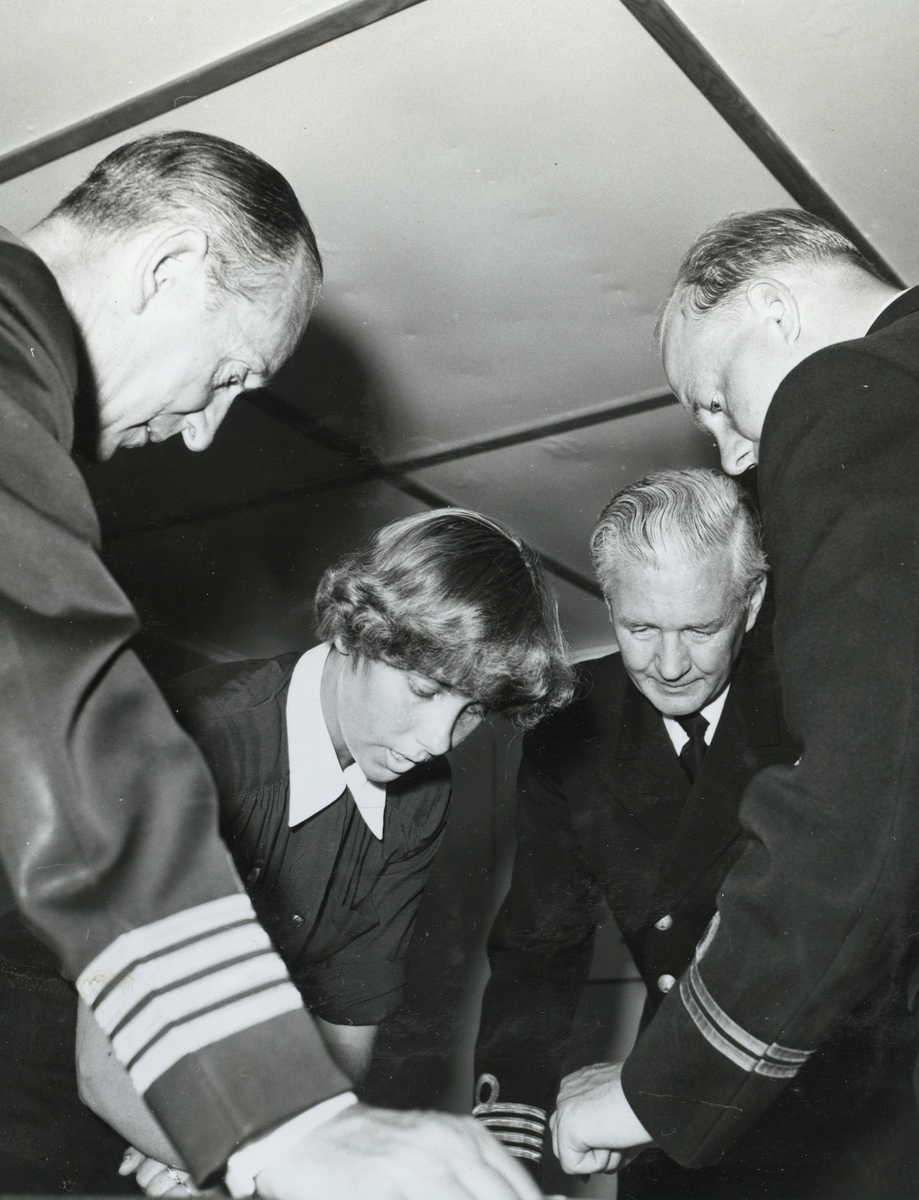 Kommendörkapten Lind af Hageby (till vänster) står tillsammas med ytterligare en kommendörkapten, en löjtnant och en lotta lutade över ett bord.