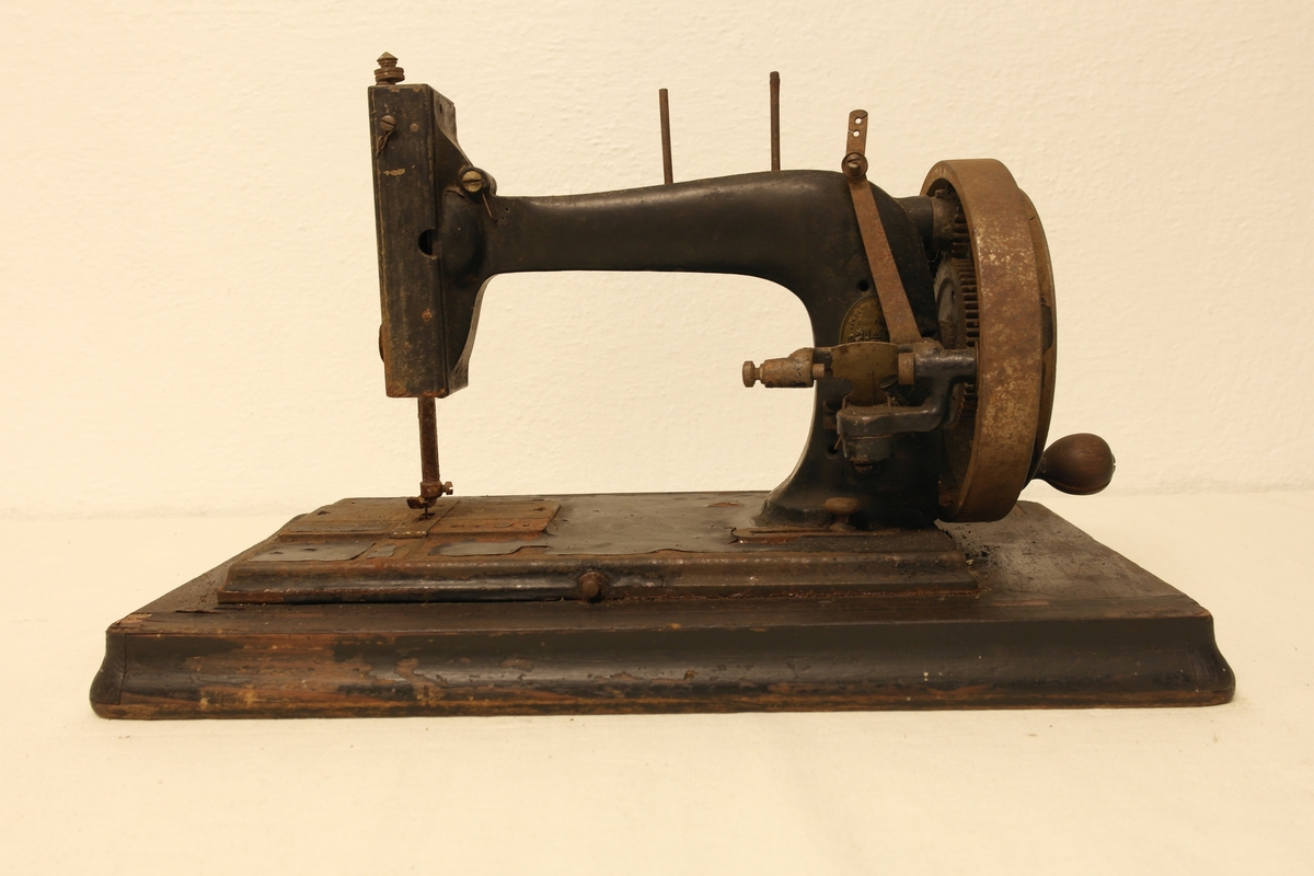 Symaskin i høvlet, pusset og beiset furu, samt støpt og malt jern. Maskinen står på ei treplate, som den opprinnelig kunne svinges opp fra. På maskinen er det fastskrudd en oval messingplate med fabrikkmerke.