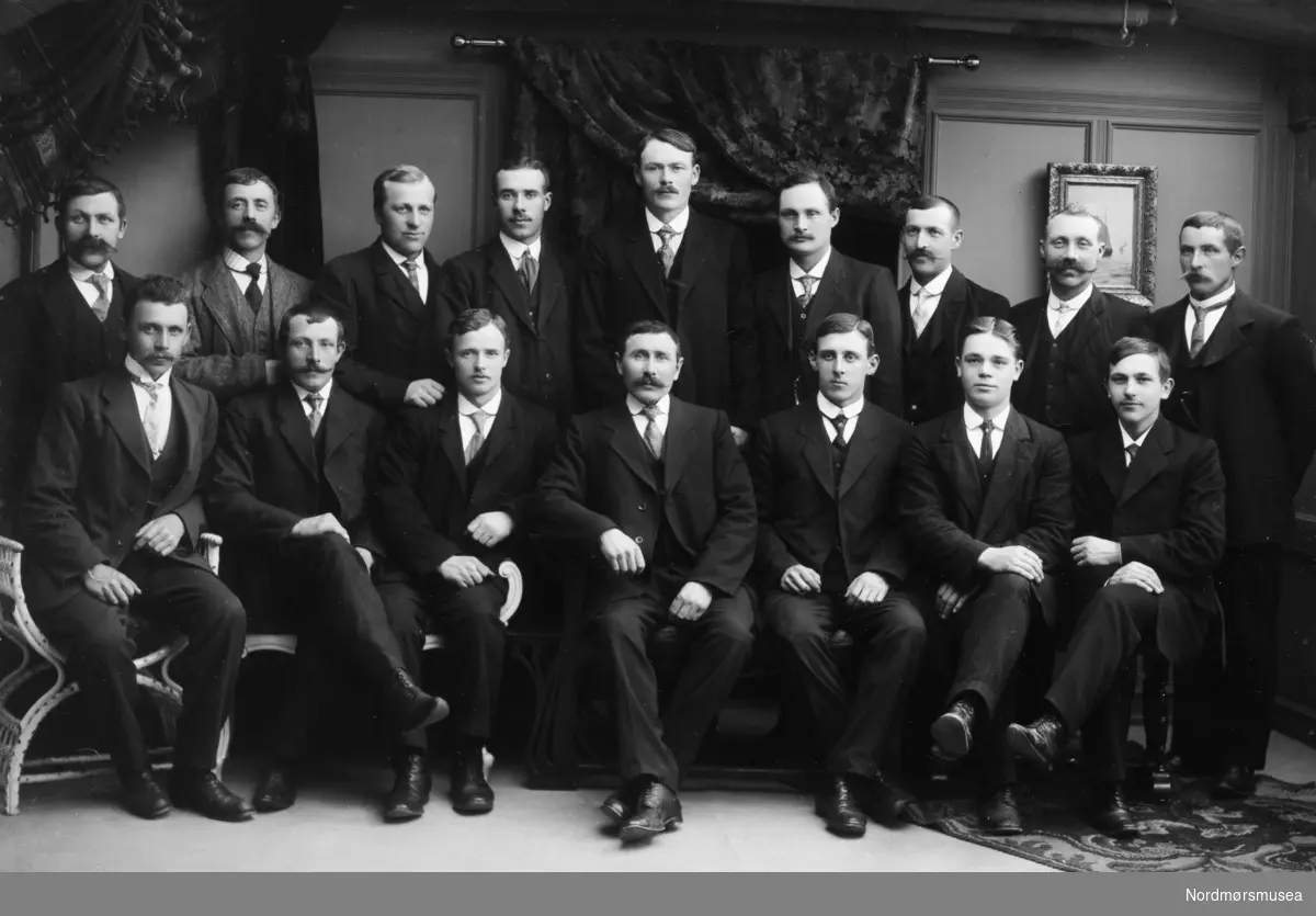 Foto av en gruppe staselig kledte menn. Det er ukjent hvem vi ser på bildet samt hvor og når bildet er tatt, men kan muligens være fra Kristiansund omkring 1910-1930. Fra Nordmøre museums fotosamlinger.