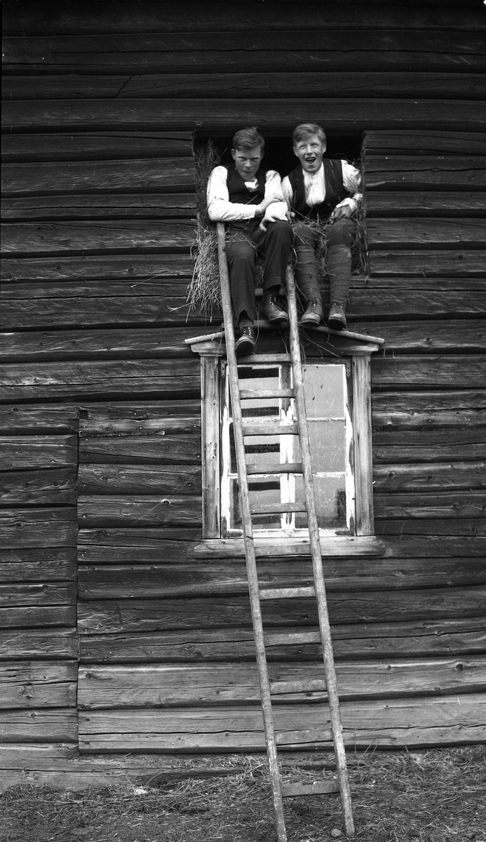To uidentifiserte unge gutter som sitter i gluggen inn til høygulvet på en låve.
