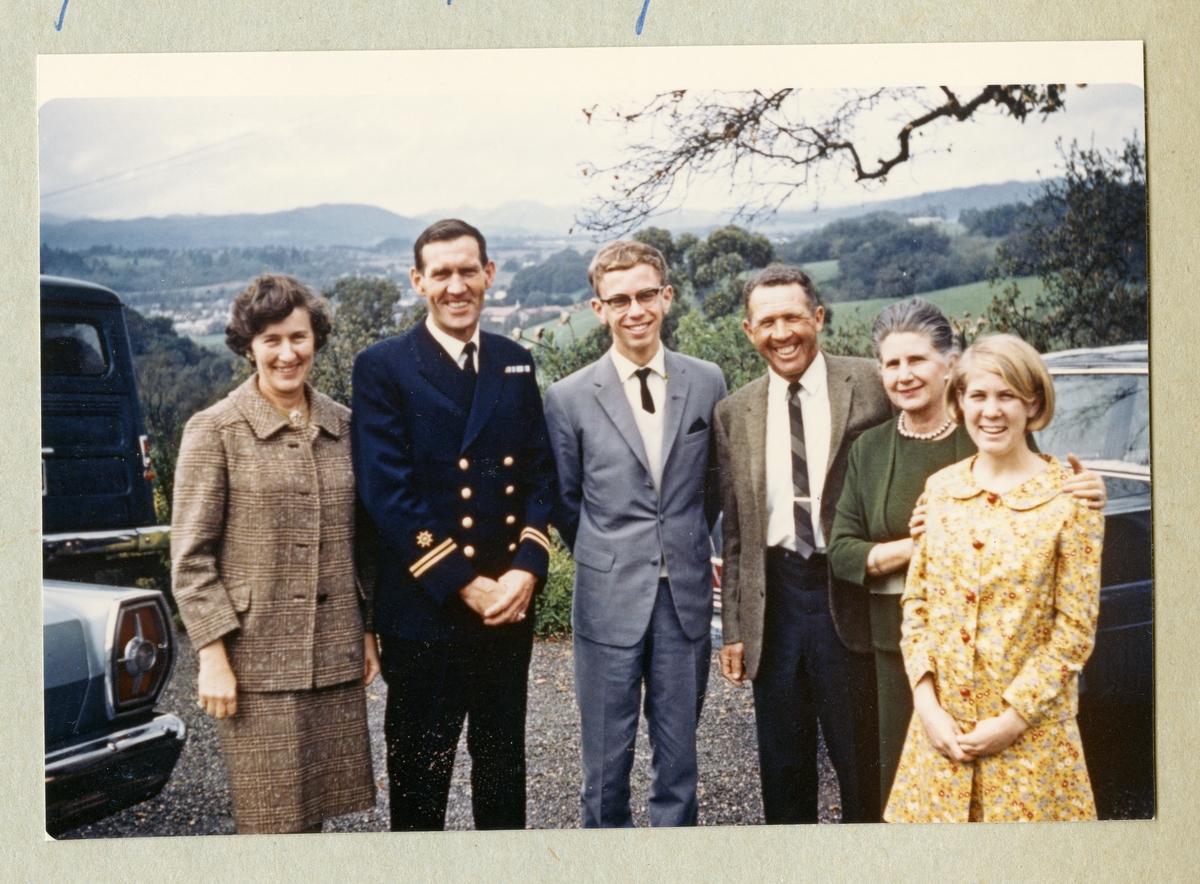 Bilden föreställer ett gruppfoto med Oskar Linde klädd i marinblå uniform tillsammans med två kavajklädda män och tre kvinnor. I bakgrunden skymtar ett grönområde. Bilden är tagen under minfartyget Älvsnabbens långresa 1966-1967.