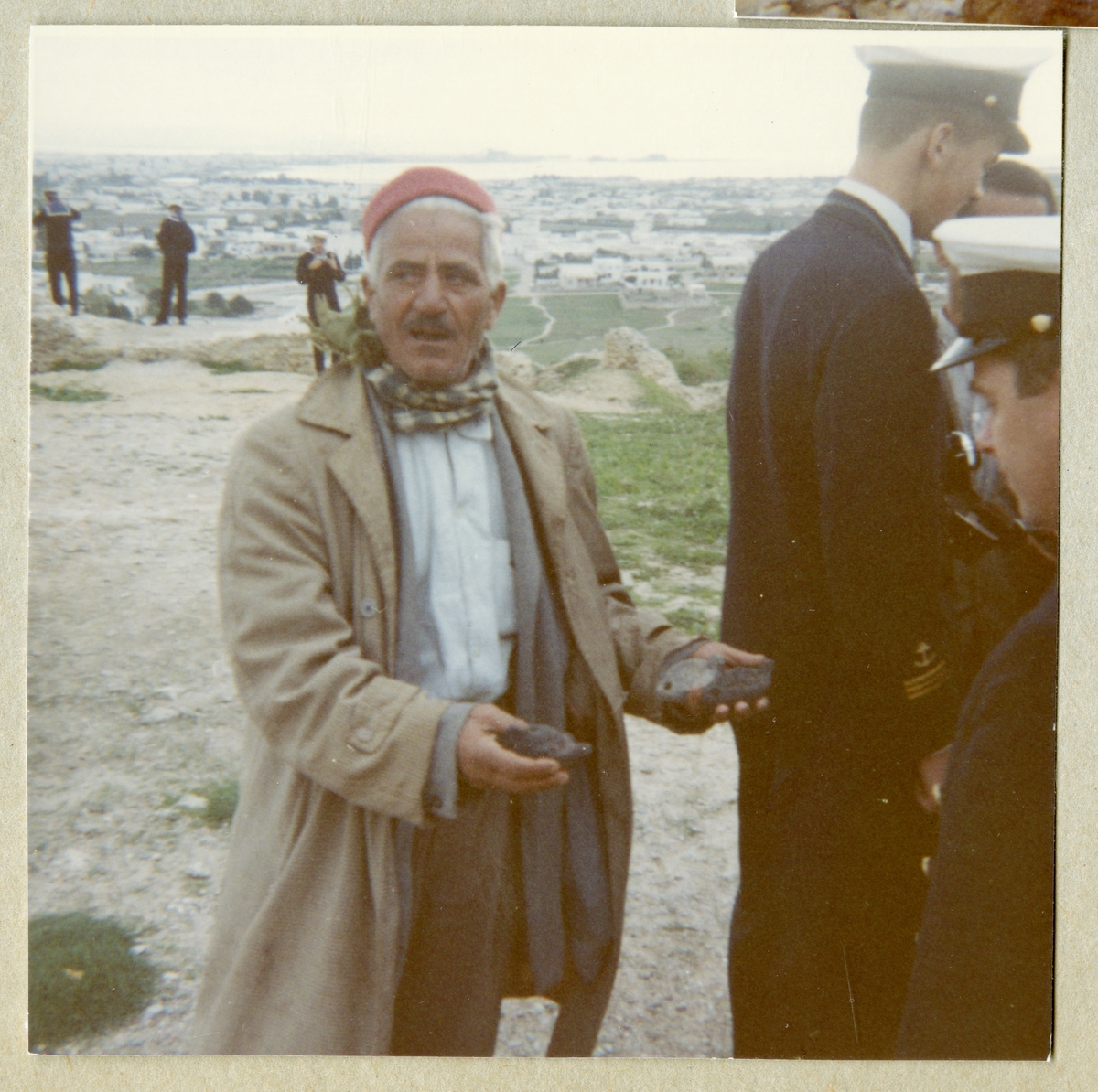 Bilden föreställer en man som visar två föremål för uniformsklädda män från Älvsnabbens besättning i Karthago under långresan 1966-1967.