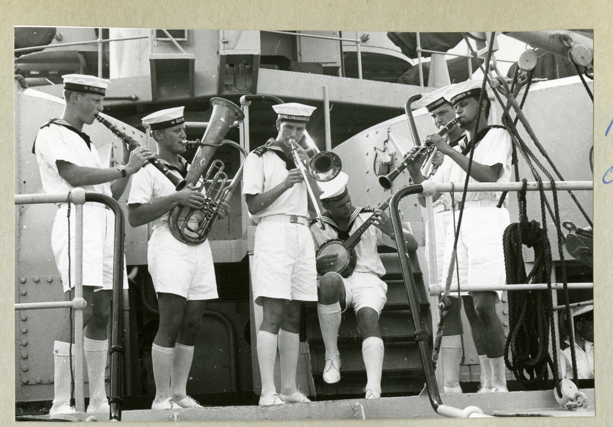 Bilden föreställer en grupp besättningsmän i sommaruniform under en julhelg ombord på minfartyget Älvsnabben. Männen spelar varsitt instument och bildar tillsammans en orkester. Bilden är tagen i samband med långresan 1966-1967.