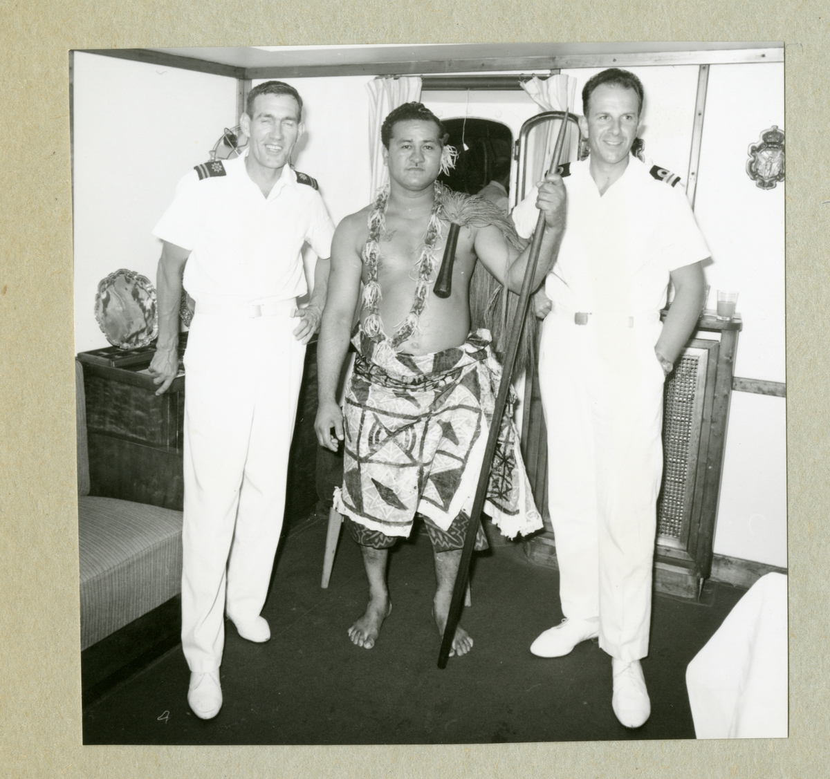 Bilden föreställer två män i vita uniformer. Mellan dem står en barbröstad man i höftskynke och med ett spjut i ena handen. Bilden är tagen under minfartyget Älvsnabbens långresa 1966-1967.