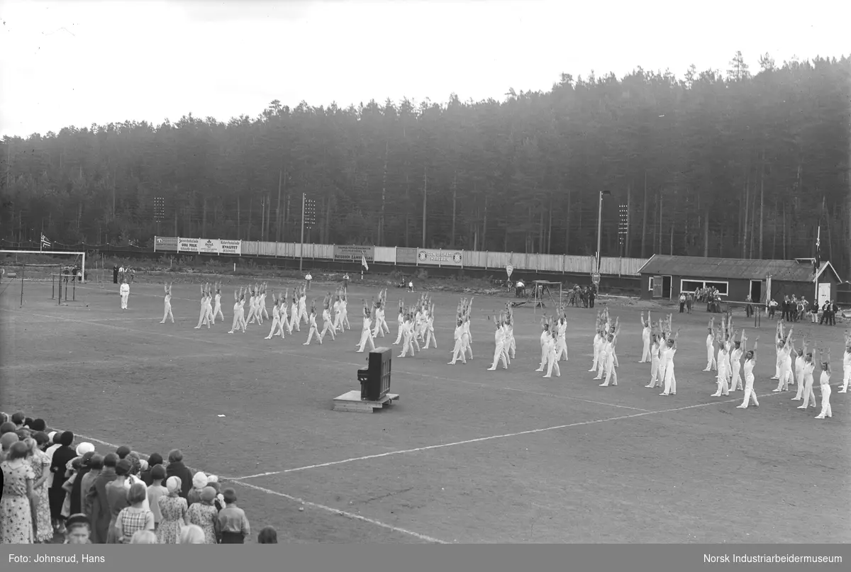 Turnstevne 1933.  Menn under turnoppvisning på stadion. Piano stående på gresset. Tilskuere rundt stadion.