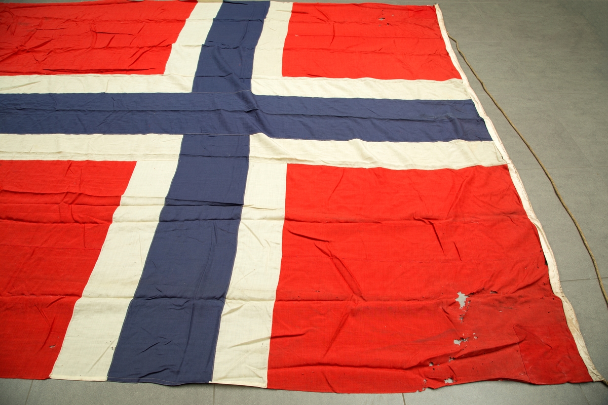 Flaggpose med flagg. A) pose i jute med tau. B) norsk flagg, meget slitt i enden motsatt stangfestet.