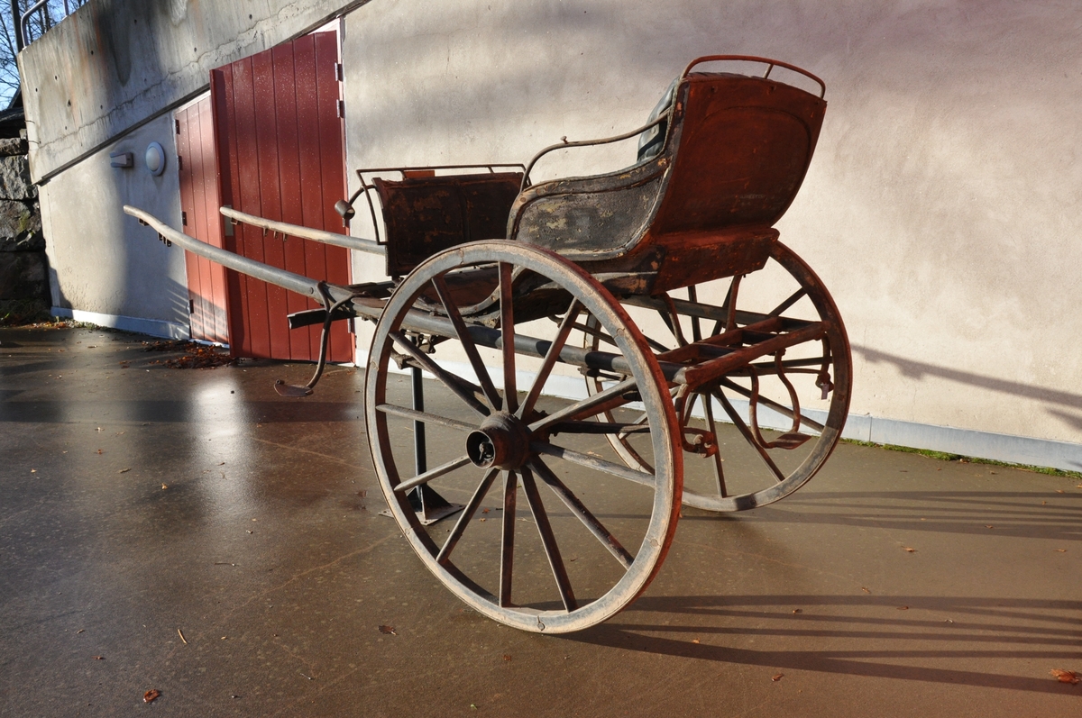 2-hjuls vogn for én hest til persontransport. Sete utført som rammeverk med fyllinger hvilende på jernbeslag.