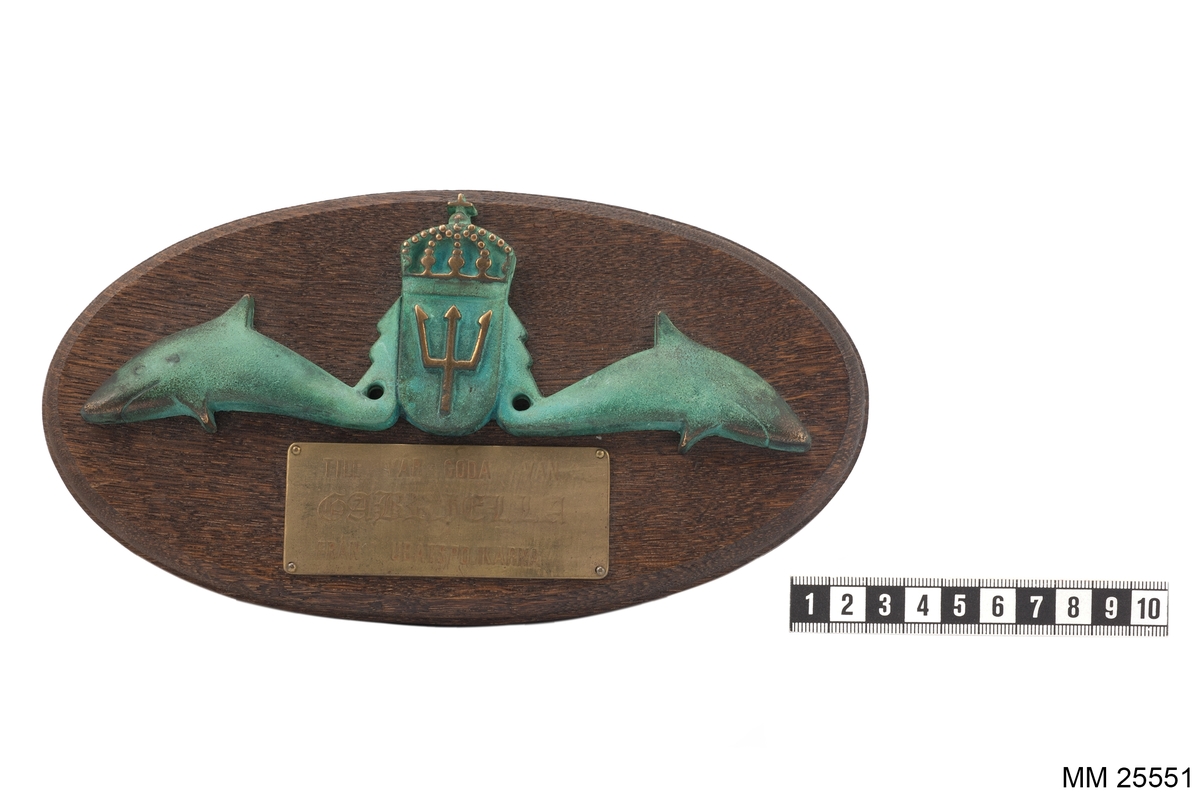 Ubåtsvapnets emblem, det vill säga två hajar som flankerar en vapensköld med Neptuns treudd, på en oval träplatta med profilerade kanter i form av ett prydnadsemblem, på emblemet finns också en bricka i brons med text.