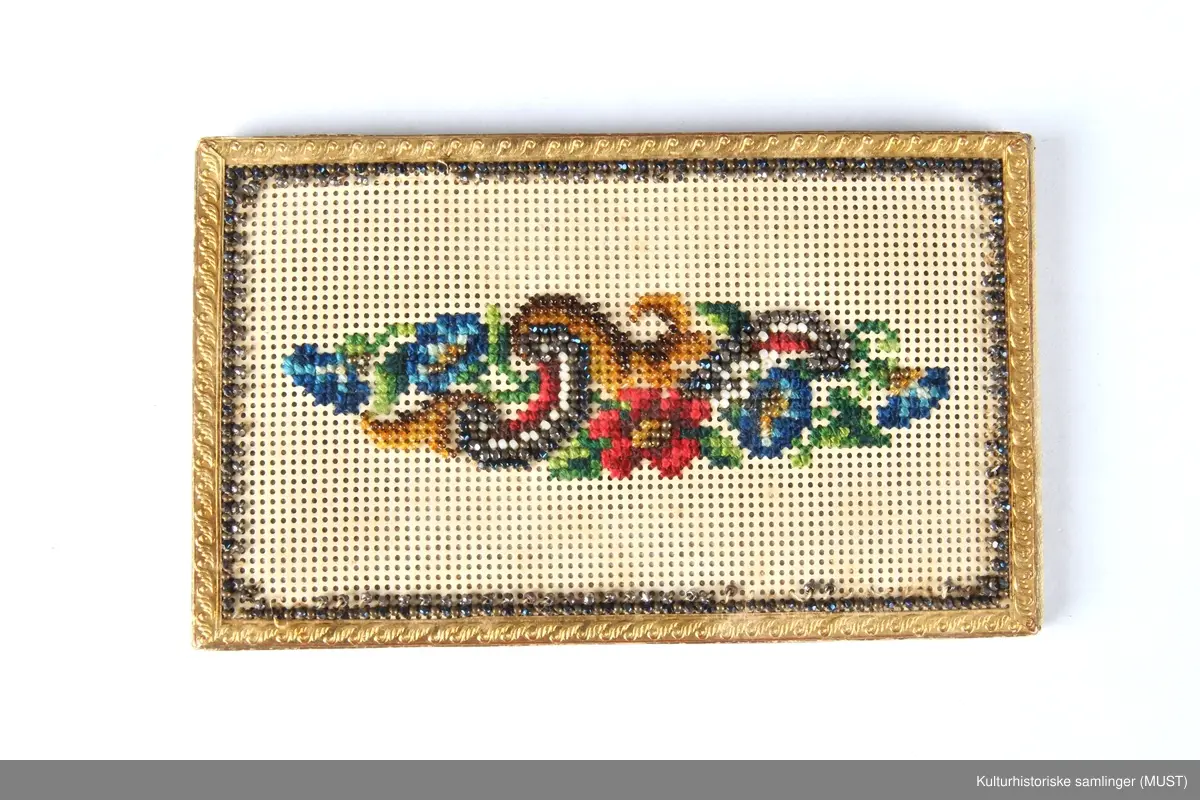 Visittkortmappe av papp. Permene består av hvit, perforert pappkartong og hvit silke. På permene korsstings- og perlebroderier, langs kanten en "gullist".