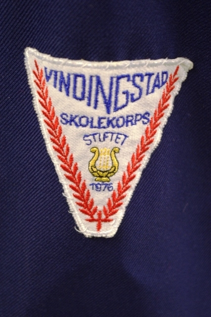 Jakke (a): blå polyester med for av blå kunstsilke. Rød krage og slag og oppslag på ermene. 3 blanke knapper. Røde epauletter med blanke knapper, rød pyntesnor rundt høre arm
Bukse (b): blå polyester, røde render i sidesømmene. Nylon glidelås i gylfen. 1 svart knapp
Magebelte (c), rødt, blankt kunstfiberstoff, foret med rød bomull. 3 folder midt på. Lukkes med borrelås. 91 l, 11.5 b
Pyntesløyfe (d), samme tøy som beltet. Røde frynser i nedkant. Kan festes med borrelås til belte. Todelt. 49 l, 12 b.