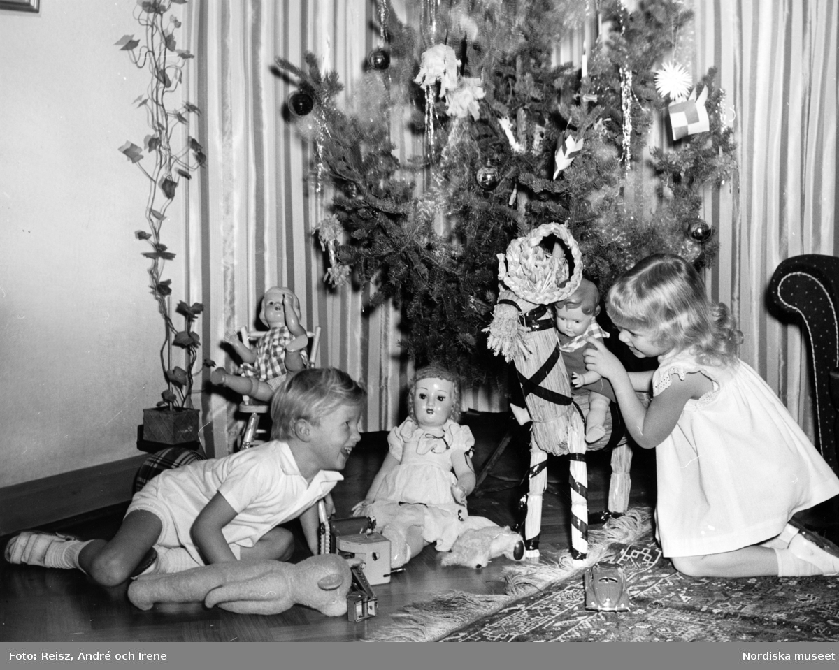 Pojke och flicka med diverse leksaker vid en julgran