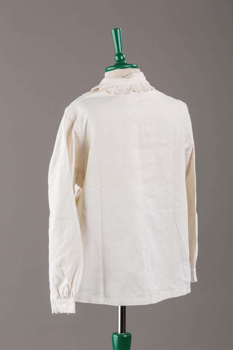 Form: Hoftelang trøye, Lange ermer, krage. Kragen og åpningen foran er kantet med  maskinprodusert blonde. Tre biser på hver side av åpn. foran. Lukkes med to løse knapper.