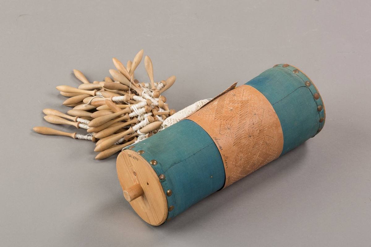 Form: Sylinderformet "pute" hvor stivt pappstykke rundt puta viser mønsteret. 
Kniplingsstykke under arbeid påspent med knappenåler
Pinner medkniplingstråd