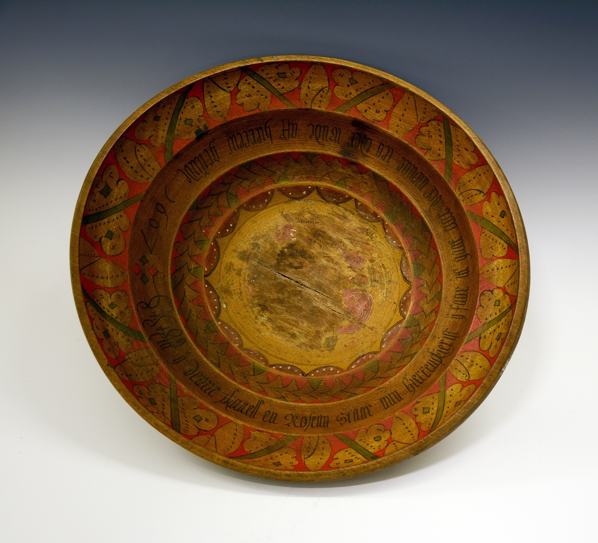 Ølbolle. Fra protokollen: Ølbolle, stor, flaagjord, svarva med 3 ribbar inni. Kromgult maala, og inni maala rosur i raudt og grønt med svart kontur og skrift. I botnen eit slag rosur, no mest burtsliten, og til borde rundt kanten eit bandsegment. I fyrste ribbe ei "myntsnor" av gule rosur, som stend paa .... I næste ribbe denne innskrifti med haag smal (minuskelsvipande) fraktur: in ij denne skaaell en Rosem Staar min hiertenskierist ij faar itt gaat aar det wonnne ieg eder ?nde aff hiertens grunde 1607. Ytste og øvste ribbe hev paa raud botn eit grønt lokastig band med gule blad og knuteformur i tidsens mynster. Under botnen stend paa 2 stadar bumerket Y utskori.