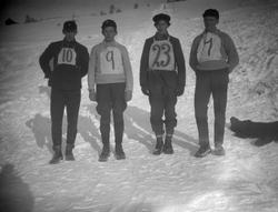 4 deltagere i hopprenn står i bakken uten ski. Nummer på bry