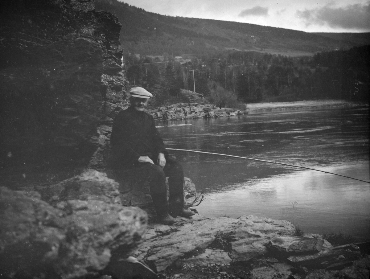 Eldre mann sitter ved elven med fiskestang.