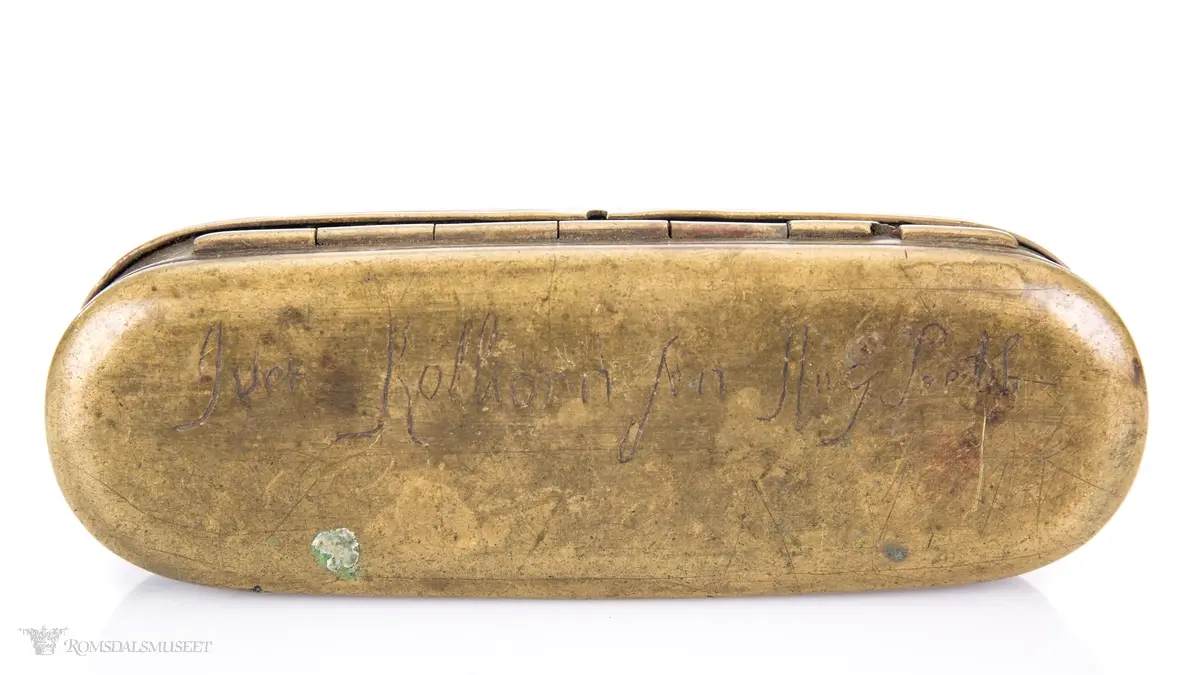 Rektangulær messingeske med avrundede ender. Har en påsatt og påklinket utenpåliggende bunn og utenpåliggende, hengslet lokk