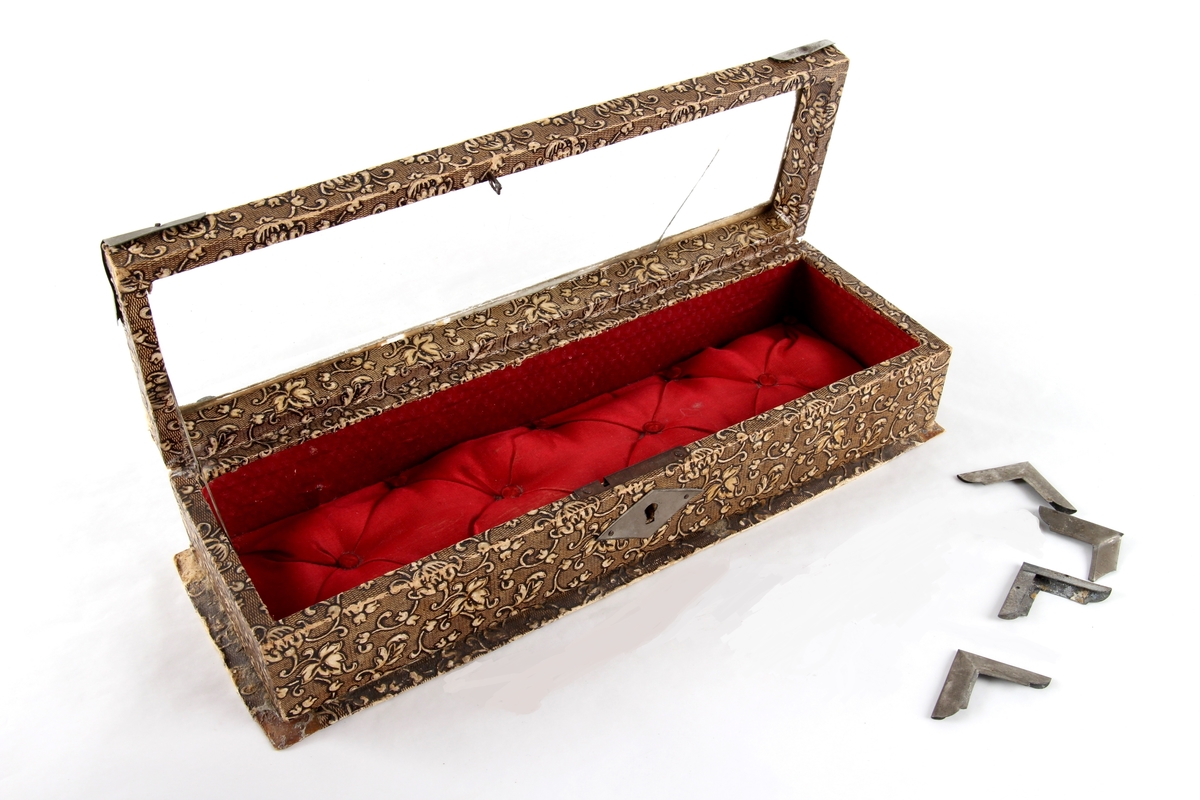 Avlangt smykkeskrin med hengsler og lokk. Lås og hjørnebeslag i metall. Lokket har et glassvindu. Foret med tekstil. Brukt til oppbevaring av små smykkegjenstander og en liten nøkkel.