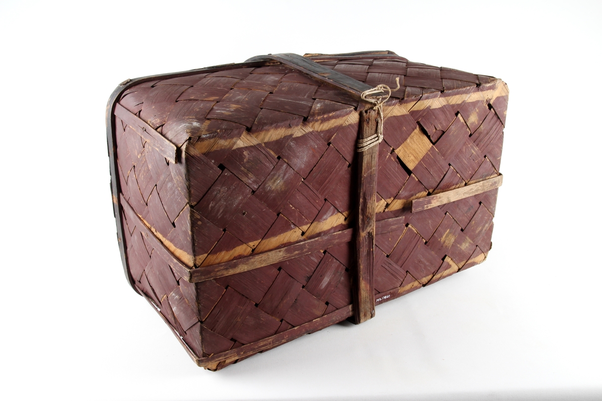 Brunmalt korg flettet av spon. En stor rund hank på midten og to lokk. Bare det ene kan åpnes.