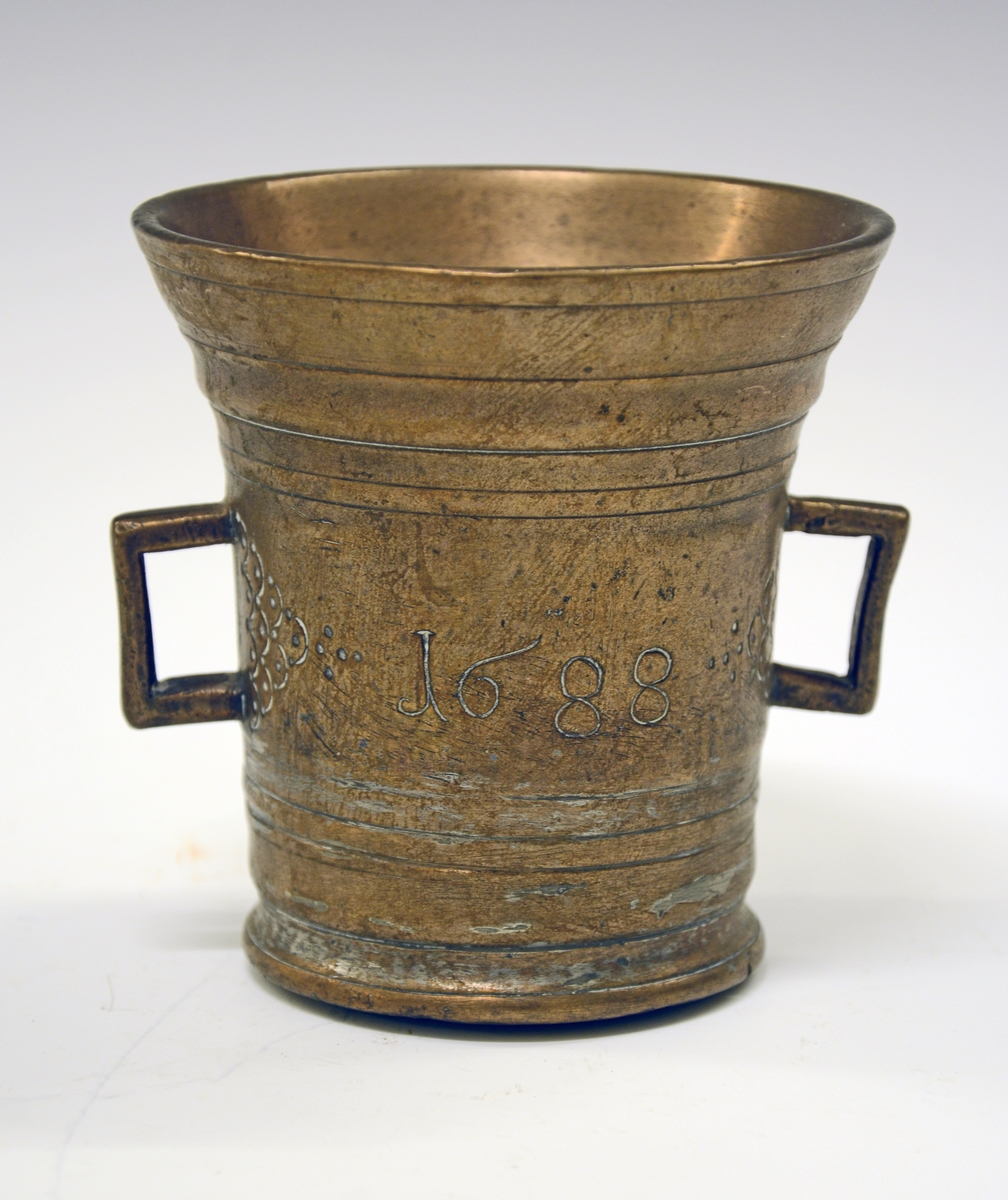 Fra protokollen:
Murte av bronse, cylindrisk, men skjæler ut uppetter; tvo henkar, støypte saman med korpus. Dreia (?) reitar rundt. Paa sidune stend i nedfeld hogst: ANNO 1688. Paa kvar side av henkane pyramide-ornament dana av halvcirklar med prikkar. Tvermaal uppe 11 cm, høgd ikr. 11 cm.