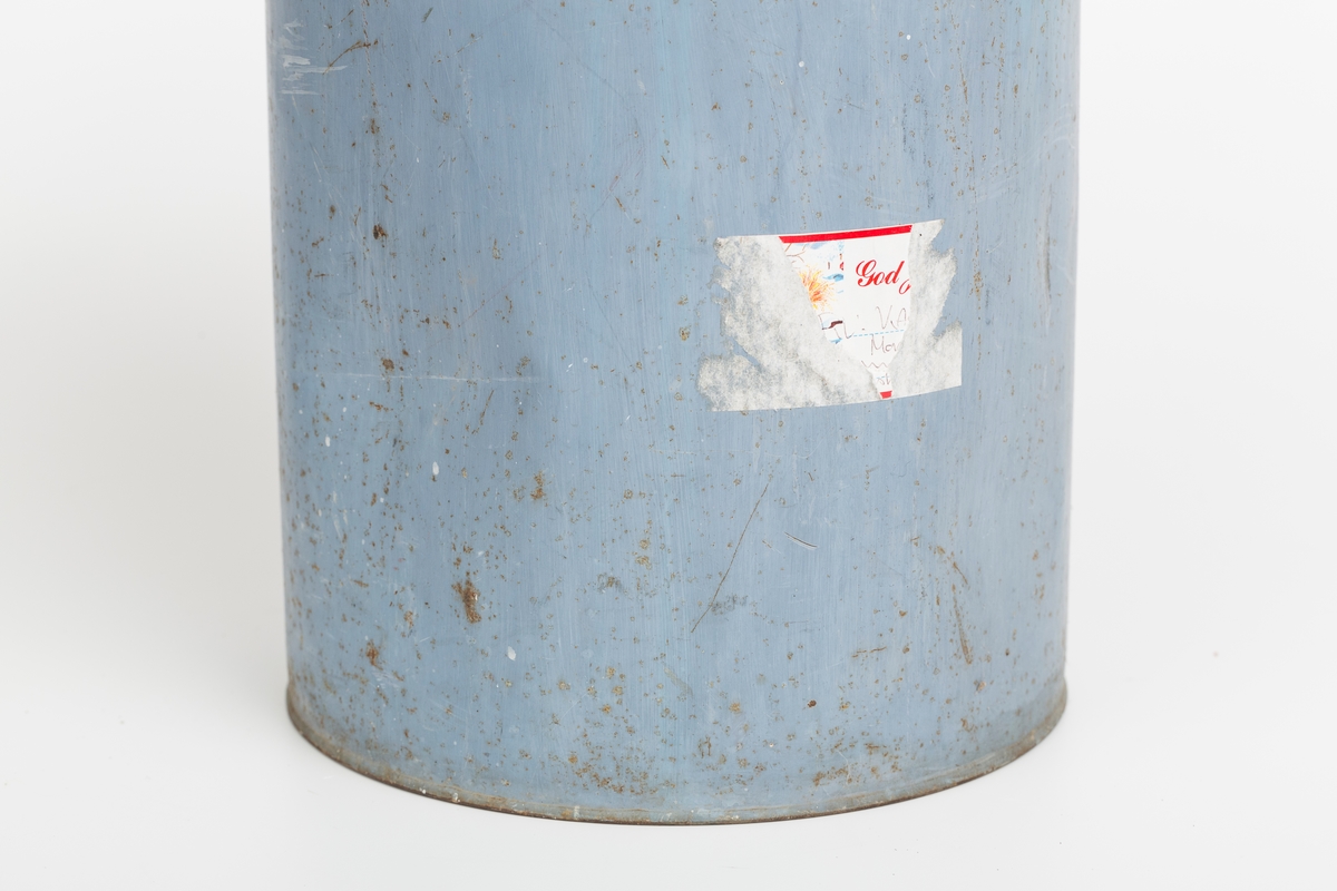 Kanne i sink, blå. Korket i tuten og korklokk med plast. Har håndtak og helletut. Kannen har påklistret god jul merkelapp med navn. Delvis avrevet.