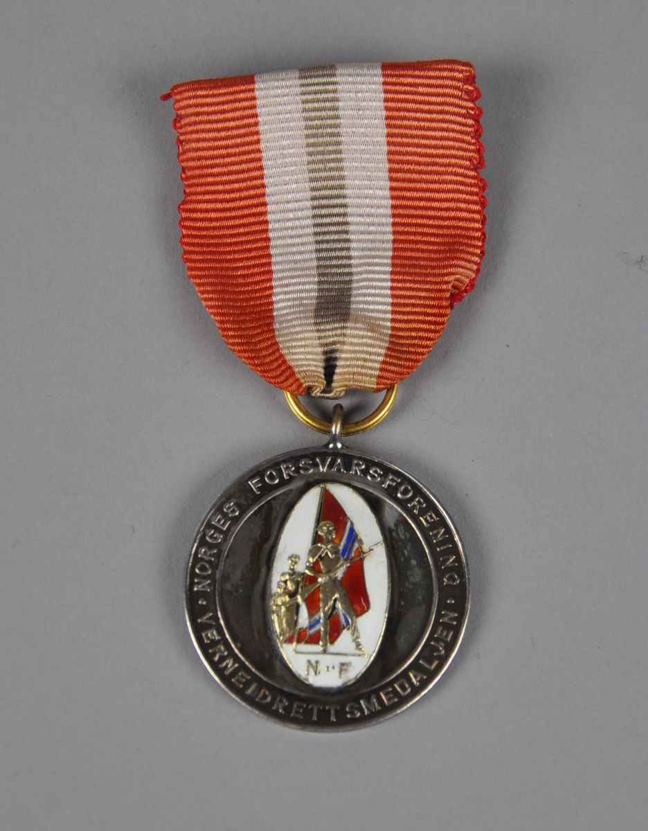 Medalje med bilde av to soldater (?) foran et norsk flagg.