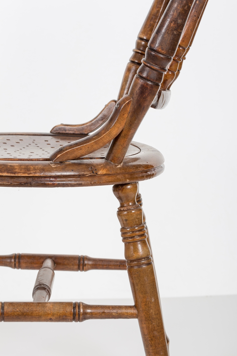 Stol i lakket treverk. Rundt stolsete med hullemønster. Rygg som er svakt buet med spiler og mønster. Dreide ben og spiler i rygg.