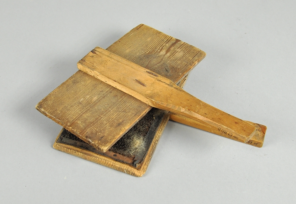 To treplater hvor innsiden av begge platene er dekket av  en skinnduk med tettsittende nåler. Begge treplatene har håndtak.