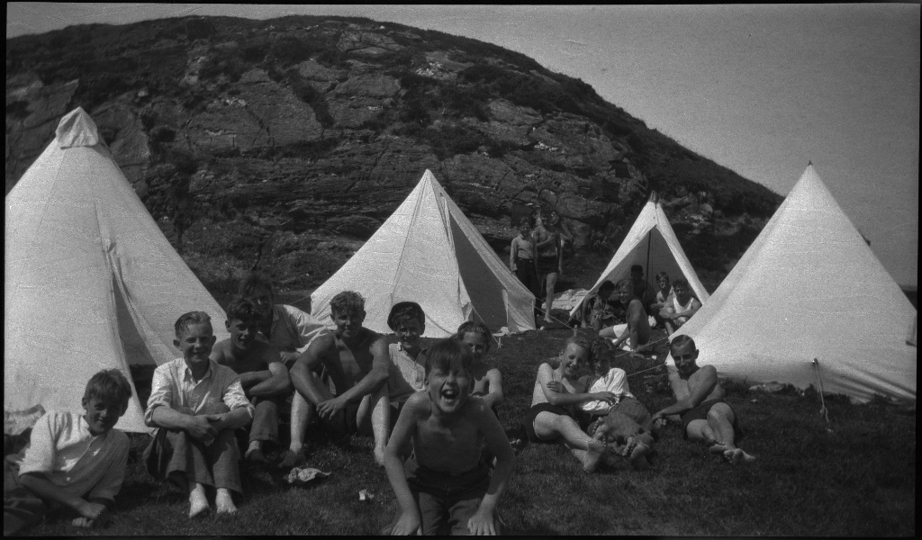 Barn og unge på og rundt stranda i Vigdelsvika. De fleste har satt opp telt, noen soler seg og noen bader. Den ene gutten på bilde nr. 6 holder et flytebelte.