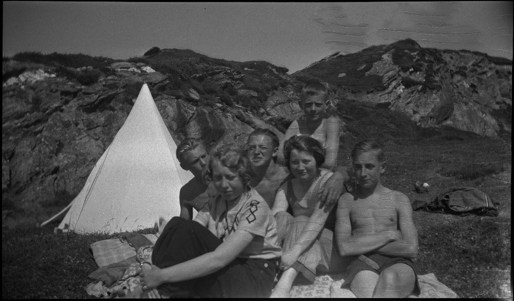 Barn og unge på og rundt stranda i Vigdelsvika. De fleste har satt opp telt, noen soler seg og noen bader. Den ene gutten på bilde nr. 6 holder et flytebelte.